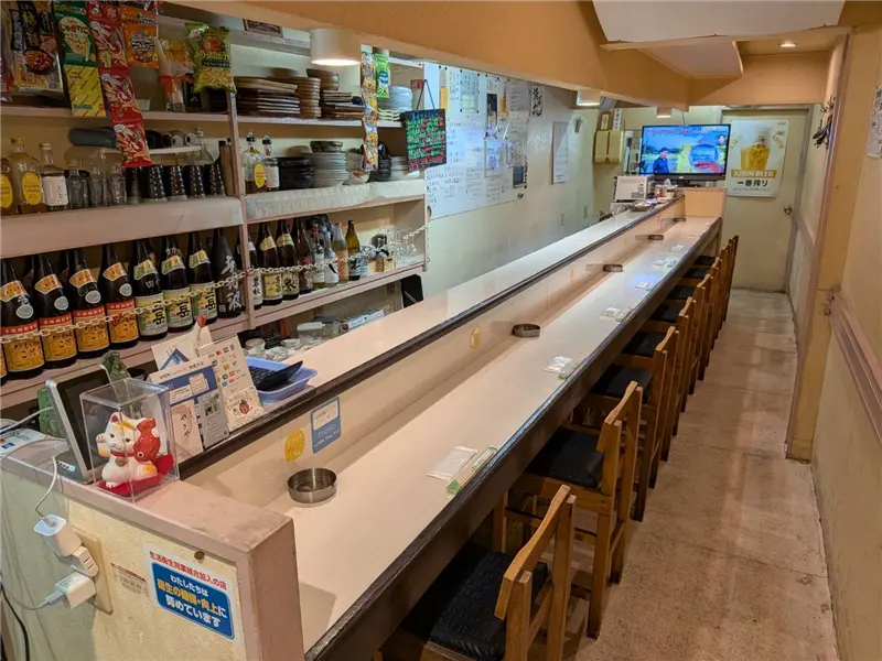 木のカウンターに並ぶ魚料理と奥まで続く居酒屋の客席