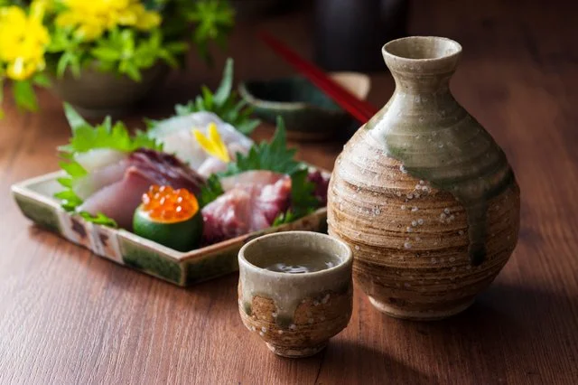 湯気の立つ魚料理と徳利が置かれた木のカウンター